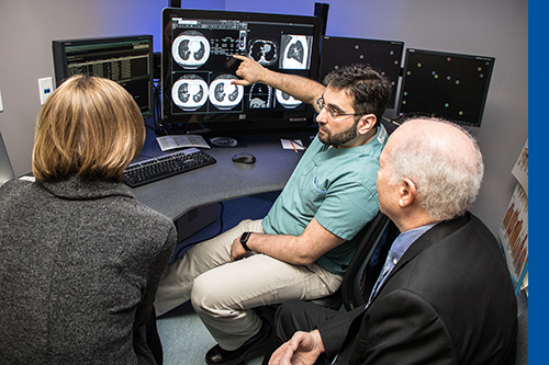 Dr. Almalki and a female and male sit around a computer screen looking at scans from a CT scanner.